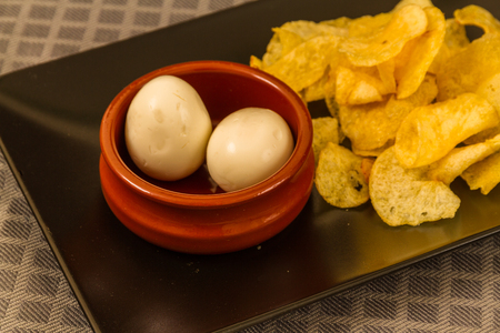 Two pickled eggs in ceramic bowl, served with crisps or chipsの写真素材
