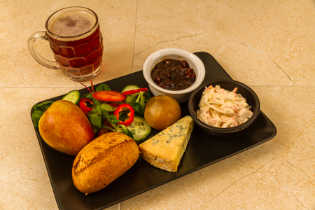 Ploughmanâs lunch with stilton cheese, pickle, pickled onion, salad, coleslaw and bread roll, apple and half pint of English ale or beer.の写真素材