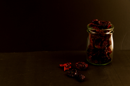 Low lit, with copy space, black area with sun dried tomatoes in jar and on surface.の写真素材
