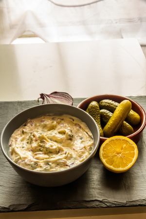 Home made tartar sauce in grey bowl with gherkins, lemon and onion.の写真素材