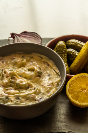 Home made tartar sauce in grey bowl with gherkins, lemon and onion.の写真素材