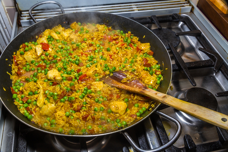 Stirring chicken paella with a wood spatula while cooking and green peas and chorizo on hobの写真素材