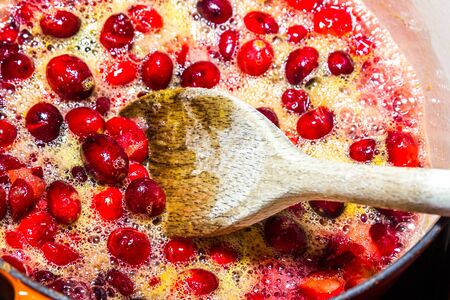 Cranberry sauce being cooked in pan, heating cranberries and orange juice with spoon, bubbling, close up.の写真素材