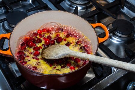 Cranberry sauce being cooked in pan, heating cranberries and orange juice with spoon, bubbling on hob.の写真素材