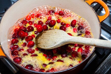 Cranberry sauce being cooked in pan, heating cranberries and orange juice with spoon, bubbling.の写真素材