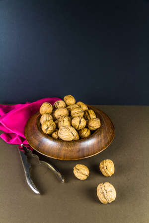 Whole walnuts piled in a wood bowl, nutcrackers on side, dark blue background, portrait from above,...