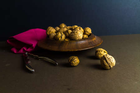 Whole walnuts piled in a wood bowl, nutcrackers on side, dark background, landscape.