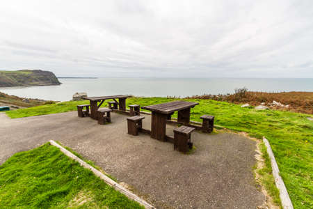 Picnic tables with sea and cliffs behind them.の写真素材
