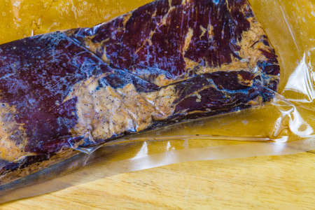 Vacuum packed Pork belly dry cured then smoked to become streaky bacon. On wooden board, landscape, close up.の写真素材