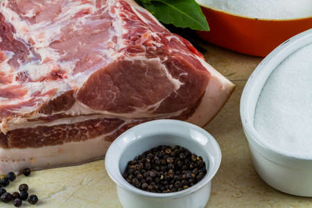 Pork loin or back joint with ingredients for dry curing into bacon, salt, sugar, peppercorns, juniper berries and bay leaves, landscape, elevated view, closeup.の写真素材