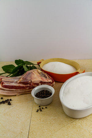 Pork loin or back joint with ingredients for dry curing into bacon, salt, sugar, peppercorns, juniper berries and bay leaves, portrait, elevated view copyspace at top.の写真素材