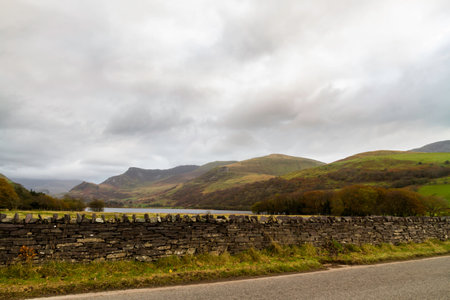 View over road to wall, Lake or Llyn Nantlle towards Drws-y-Coed with Snowdon or Yr Wyddfa under cloud, landscapeの写真素材