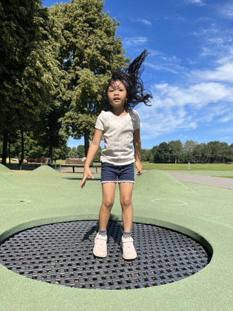 Little girl jumping on a trampoline in a public park.の写真素材