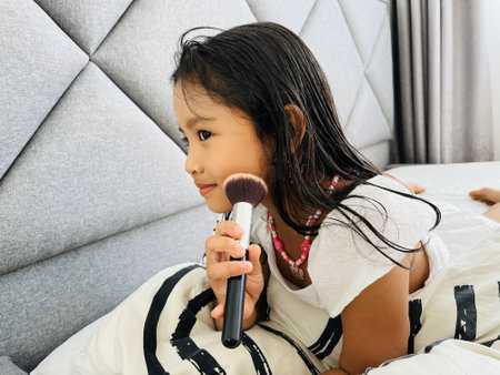 Cute asian little girl applying powder on her face with makeup brushの写真素材