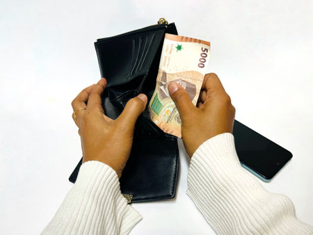 Woman's hands holding a wallet take Indonesian money on a white background. Hands open the leather wallet. 5000 rupiah in the walletの写真素材