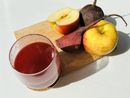 A glass of beetroot mix with apple juice on a wooden board with fresh fruits on the tableの写真素材