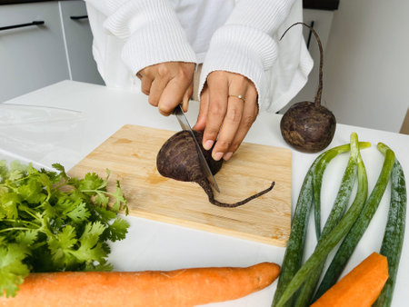 Woman's hands cutting beetroot on a wooden board in the kitchenの写真素材