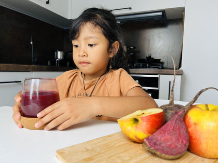 Cute asian little girl holding a glass of fruit juice in the kitchenの写真素材