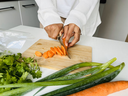 Woman cutting carrots on a chopping board in the kitchen at home. Healthy eating and dieting...