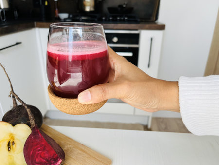 Woman's hand holding a glass of beetroot smoothie in the kitchenの写真素材