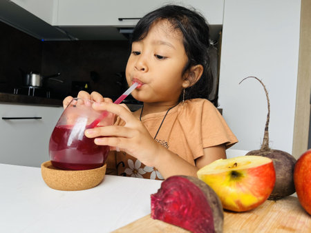 Little girl drinking beetroot and apple juice in the kitchen at home. Healthy eating concept.の写真素材