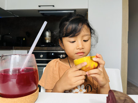 Asian little girl eating apple in the kitchen at home. Healthy food concept.の写真素材