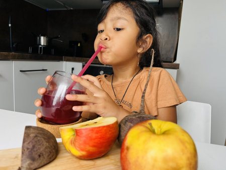 Little girl drinking beetroot and apple juice in the kitchen at home. Healthy eating concept.の写真素材