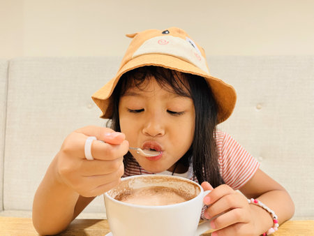 Cute little Asian girl eating delicious hot cocoa or chocolate drinking in white cup and sloppy for breakfast in the morning on table cafe restaurantの写真素材