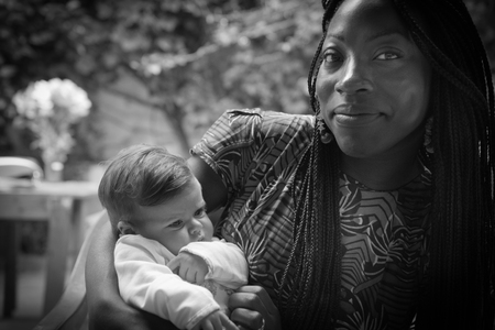 An afro-american girl is holding a caucasian newborn with tenderness .の写真素材
