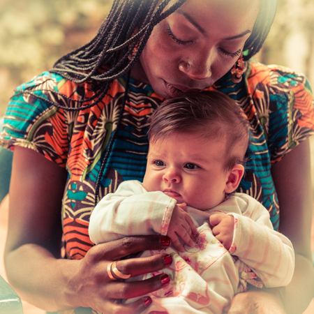 An afro-american girl is holding a caucasian newborn with tenderness .の写真素材