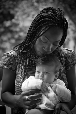 An afro-american girl is holding a caucasian newborn with tenderness .の写真素材