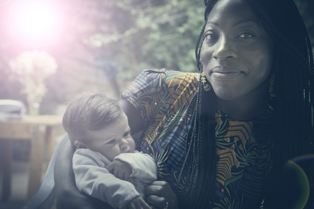 An afro-american girl is holding a caucasian newborn with tenderness .の写真素材