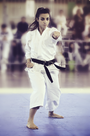 A black belt girl is performing a kata at a karate competition. People out of focus in background.の写真素材