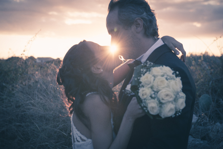 A newlymarried couple are kissing ; the sun appears bewteen them in the wonderful location of the Plemmirio Park in Siracusa (Sicily).の写真素材