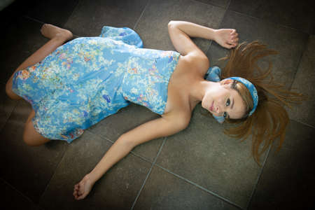 A girl 16 y old is wearing a light blue dress and laying on the ground with spread arms.の写真素材