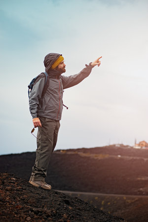 Hiker with backpack standing on top of the mountain and pointing awayの写真素材