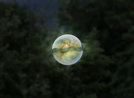 A amazing one colourful bubble from bubble blower flyin in the air on dark background. Amazing detail. Circle. Blue, yellow, orange, greenの写真素材
