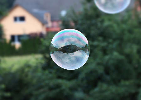 A one big bubble flying in the air. Bubble serve as mirror so we can see some house and cloudy....