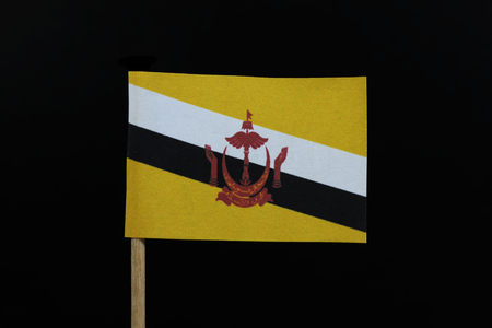 A official and unique  flag of Brunei on toothpick on black background. A centered red crest of Brunei on a yellow field cut by black and white diagonal stripes.の写真素材
