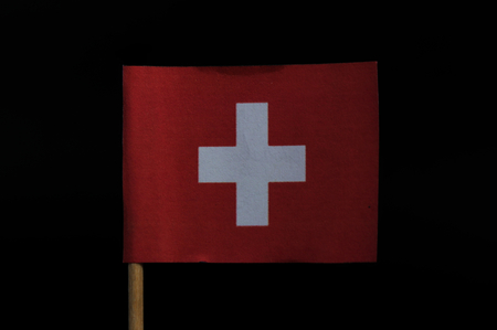 A wonderful and original national flag of Switzerland on toothpick on black background. A square flag with a white cross in the centre and background in red.の写真素材