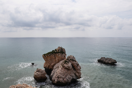View on AphroditeÂ´s rock from bigger hill on Petra tou romiou beach. Incredible clear water in mediterranean sea with cloudy sky. Incredible famous place Rock of Greek nearby Kouklia in Cyprus.の写真素材