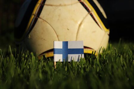 Finland flag stick to grass with football ball in background. Soccer championship 2022.  Blue and white paper on wooden stick. Finnish state symbol. International action.の写真素材