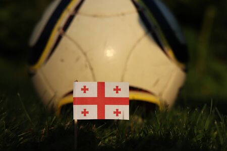 National flag of Georgia on wooden thick stick stabbed in soccer field and in the background classic football ball. World Championship 2022.の写真素材