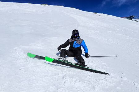 Pro skier in winter outfing lying or sitting in white snow with his black and green skis. Male skier after falling down on a mountain slope. Ski crashの写真素材