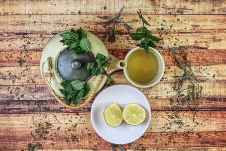 Teapot full of salvia tea with honey and cup of warm drink and beside plate with two slice of lemons. For kept healthy and refill some important vitamines. Concept of healthy, modern apothecary.の写真素材