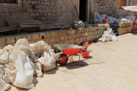 A construction site under construction in the middle old town Dubrovnik. Building new path. Worker repair damaged parts of wall and castle. Bags with sand, bricks, tools for job, bucket. Croatia.のeditorial素材