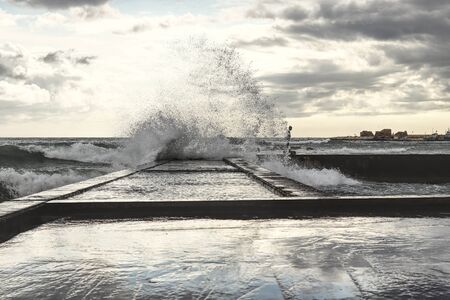 Huge spray of sea water flies into the air and envelops a beautiful sunset for a while. Mother Nature rebels against human activities. The destructive power of the sea. Paphos, Cyprus, South Europe.の写真素材
