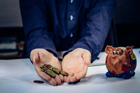 Thoughtful serious young financial adviser sit at home office desk with coins and notepad thinking...