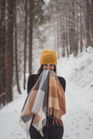 Young woman aged 20-24 with blue eyes trying to keep warm in gold fortuna winter jacket. Exuberant girl smiles from wonderful winter around her. Casual portrait in winter. Fashion shoot while snowing.の写真素材