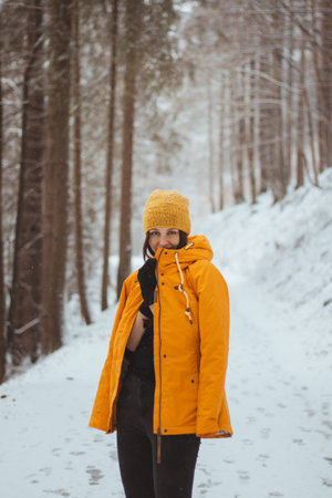 Young woman aged 20-24 with blue eyes trying to keep warm in gold fortuna winter jacket. Exuberant girl smiles from wonderful winter around her. Casual portrait in winter. Fashion shoot while snowing.の写真素材